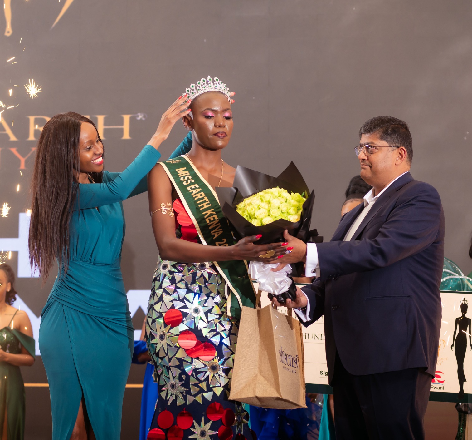 Pwani Oil's Head of Marketing, Caroline Ntinyari (L), crowns Faith Wanyama (C) as Miss Earth Kenya 2024 as Pwani Oil's Commercial Director, Rajul Malde (R), presents her with a bouquet of flowers to celebrate her victory. PHOTO/COURTESY