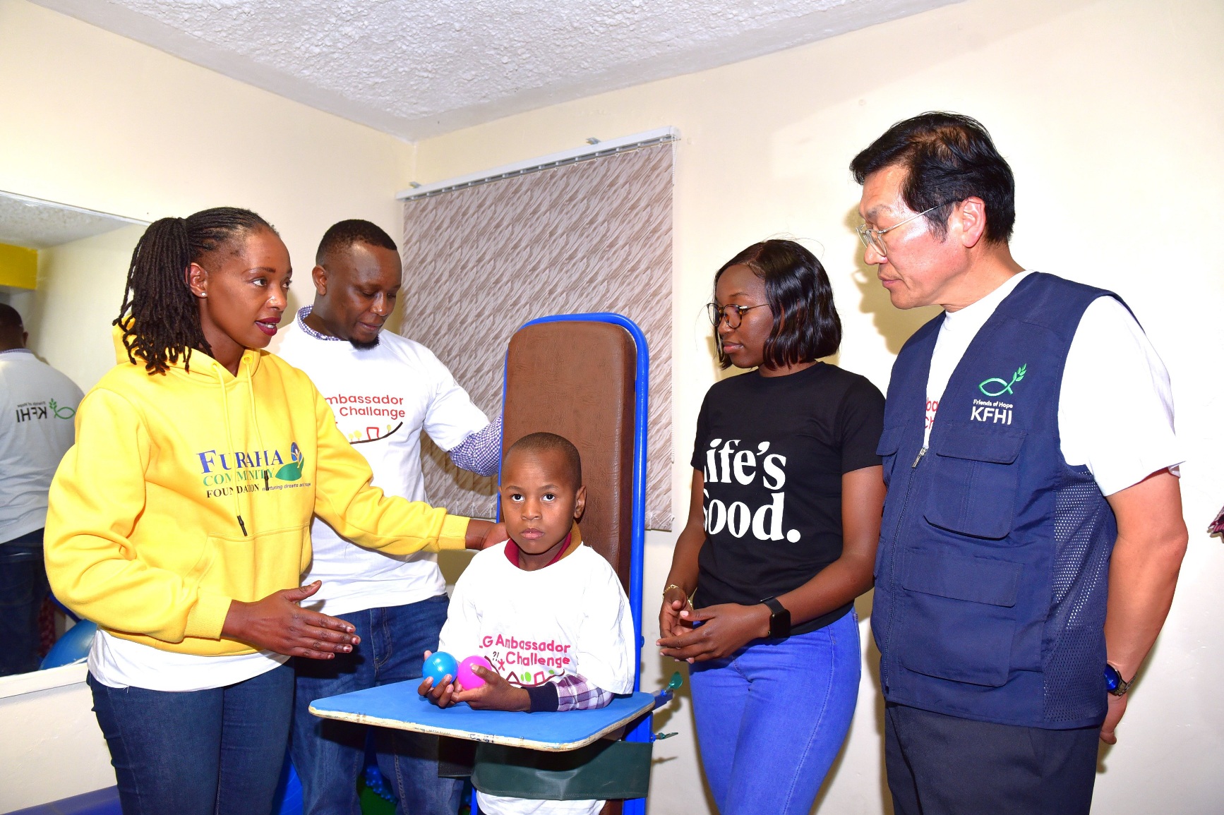  (L-R), Furaha Community Foundation School Nurse Lydia Muchoki demonstrates the use of a physiotherapy standing frame with pupil Godwin Odeng. Observing are Furaha Community Foundation Co-Founder and Executive Director David Oginga, LG Electronics EA PR and CSR Lead Glenda Achieng, and KFHI Director Chun Jong Hu. The physiotherapy equipment will benefit up to 30 disabled children. The Furaha Community Foundation, an NGO established in 2005, has been supporting needy children but faced challenges in assisting those with disabilities due to a lack of appropriate equipment. PHOTO/COURTESY